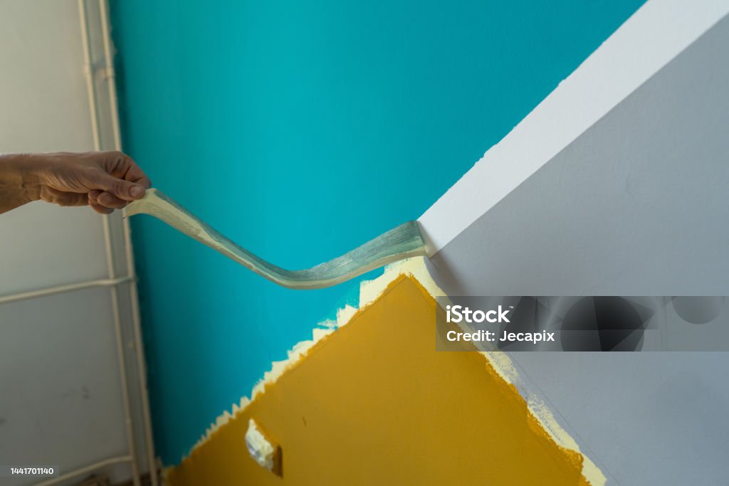 Woman's hand removing masking tape after finished painting the wall.
